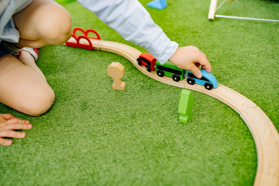 A young child plays with a colorful wooden toy train set on green grass.