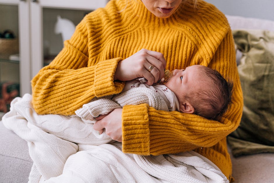 A mother lovingly holds her newborn baby, wrapped in a blanket, wearing a yellow sweater indoors.